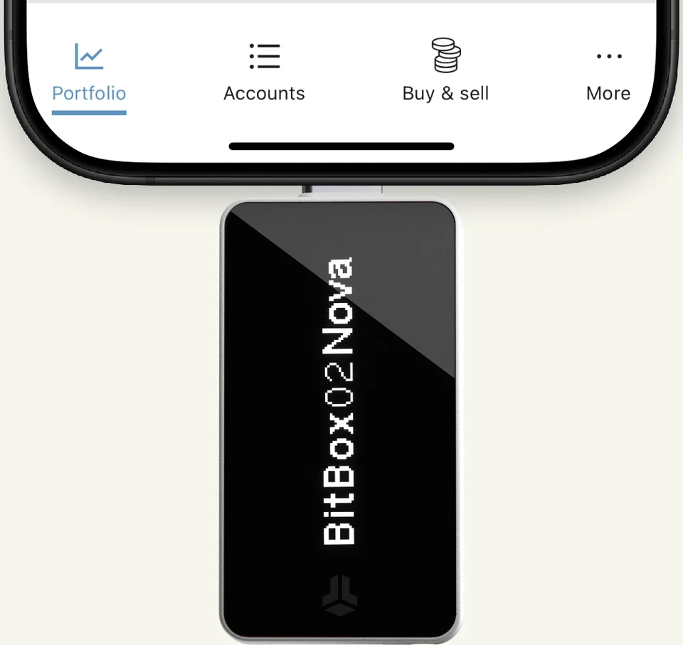 BitBox02 Nova plugged into the bottom of an iPhone, with part of BitBoxApp visible.