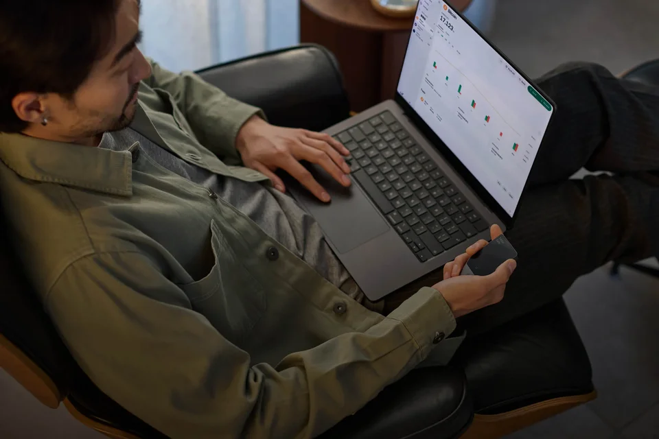 A person using a laptop while holding a Trezor Safe 7.