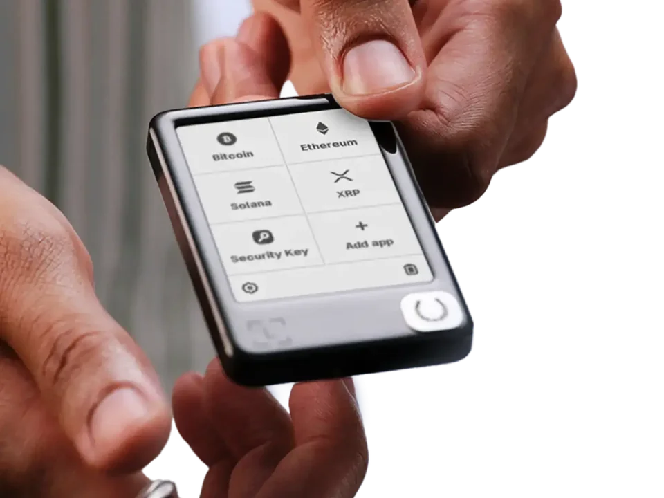 Ledger Nano Gen5 held between two hands, with its monochrome app menu visible.