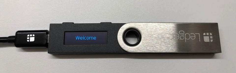 Original Ledger Nano S connected by micro-USB, with Welcome on its small screen.