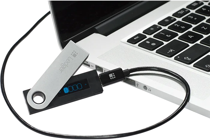 An original Ledger Nano S connected to a laptop by USB.