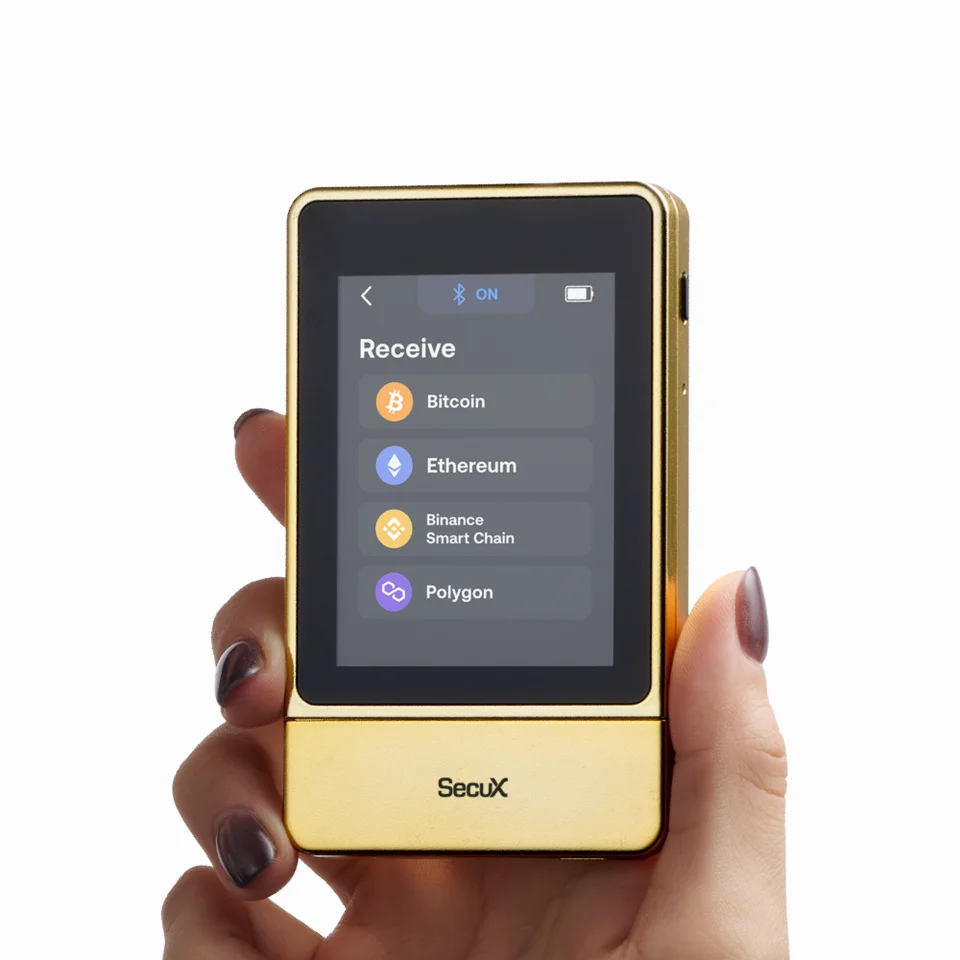 A hand holds the gold-finished SecuX NeoGold, with Bitcoin, Ethereum, BNB Smart Chain and Polygon listed in the Receive menu.