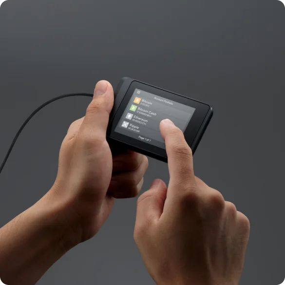 Hands hold a USB-connected SecuX W10; a finger touches its touchscreen account list.